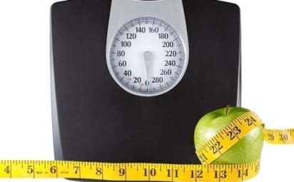 Floor scale with tape measure wrapped around apple to illustrate obesity